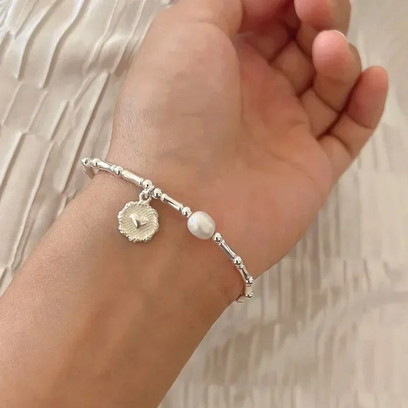 Silver bracelet with a pearl charm on a wrist against a neutral background