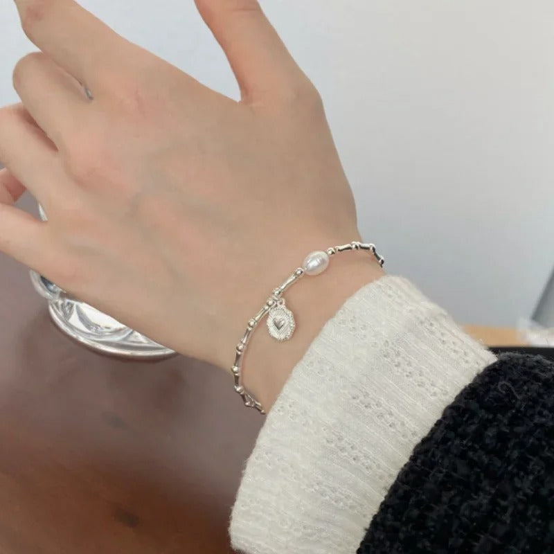 Close-up of a hand wearing a silver bracelet with a heart charm on a blurred background