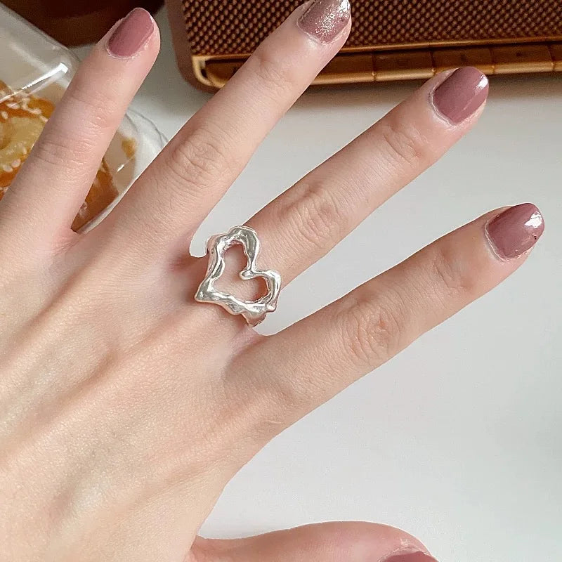 Hand wearing a silver ring with a heart design on a neutral background