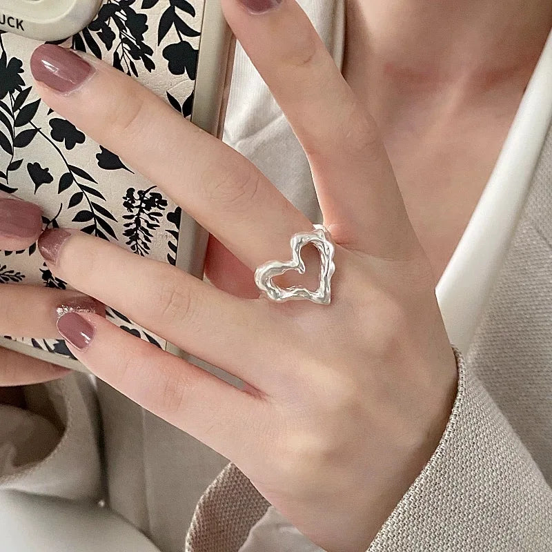 Hand wearing a silver heart-shaped ring with a blurred background