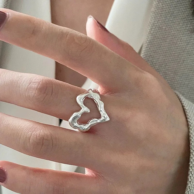 Silver heart-shaped ring on a person's finger with a neutral background