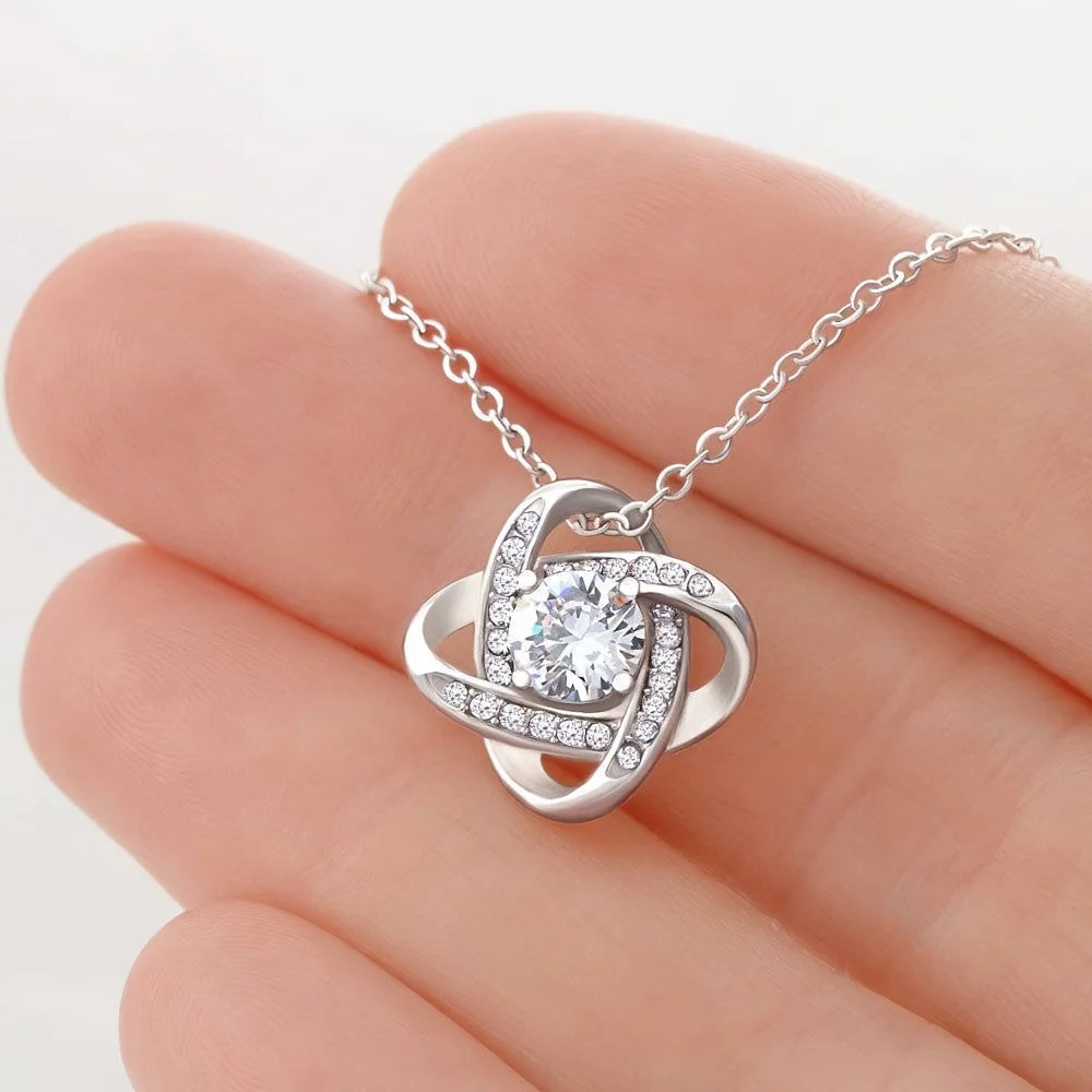 Silver necklace with a diamond pendant held between fingers on a white background