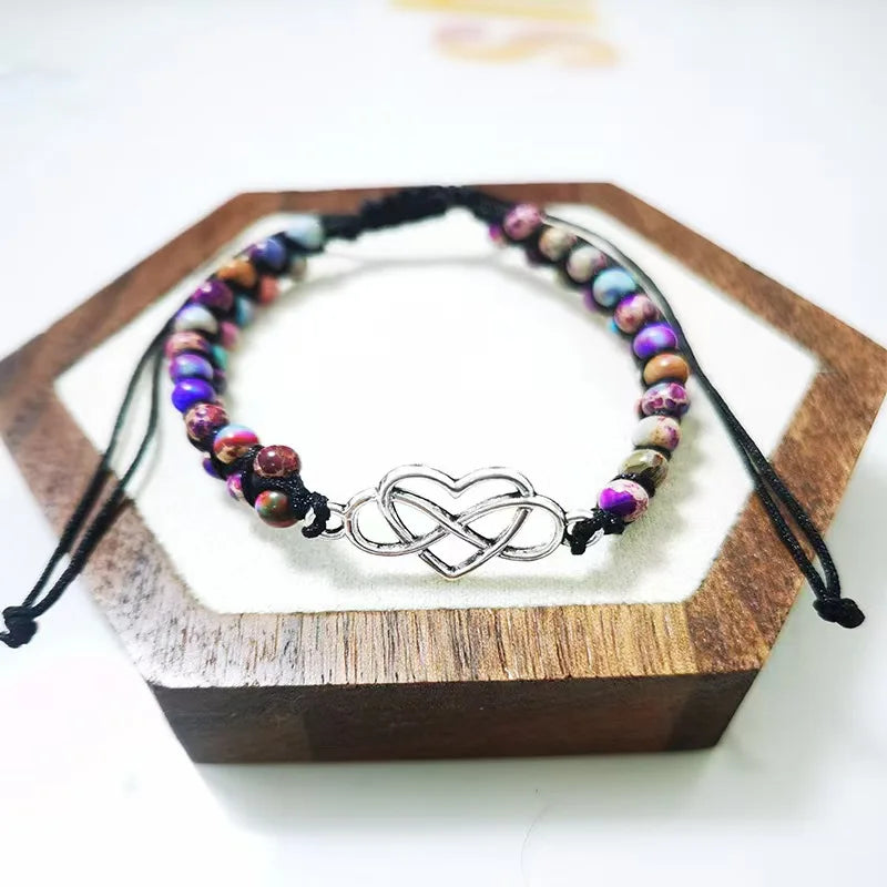 Multicolored beaded bracelet with an infinity symbol charm on a wooden stand.