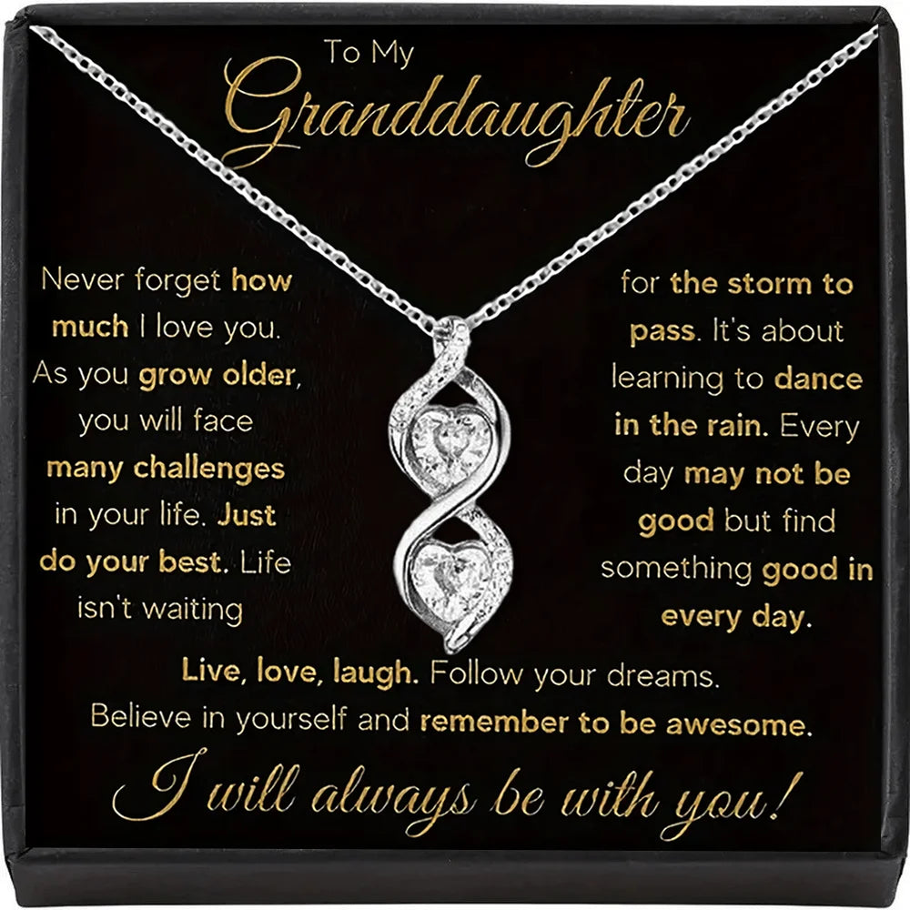 Silver necklace with heart pendant on a black card with gold text, displayed in a box.