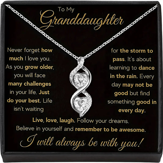 Silver necklace with heart pendant on a black card with gold text, displayed in a box.