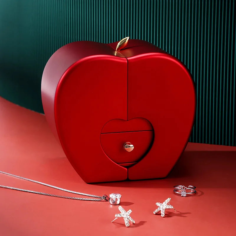 Red apple-shaped jewelry box with jewelry on a red surface
