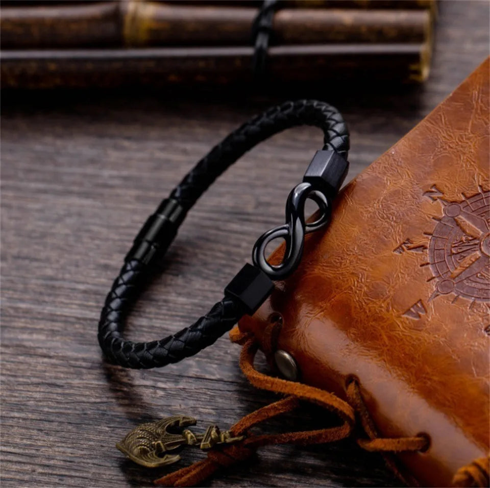 Black braided leather bracelet with a metal clasp on a wooden surface with a leather book.