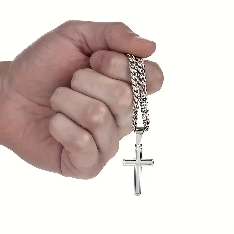 Hand holding a silver chain with a cross pendant on a white background
