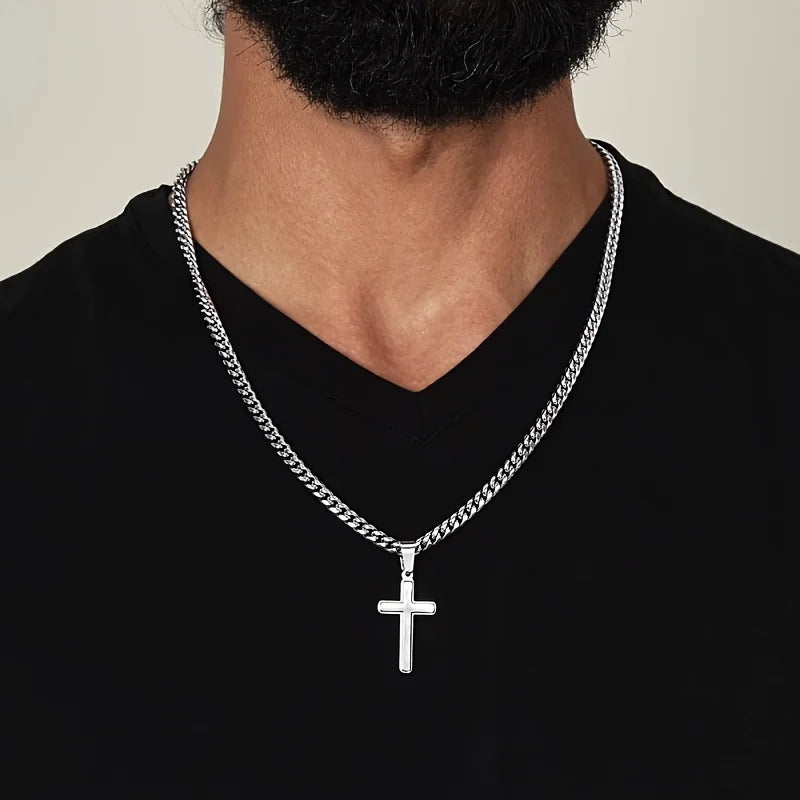 Silver chain necklace with a cross pendant worn by a person on a plain background