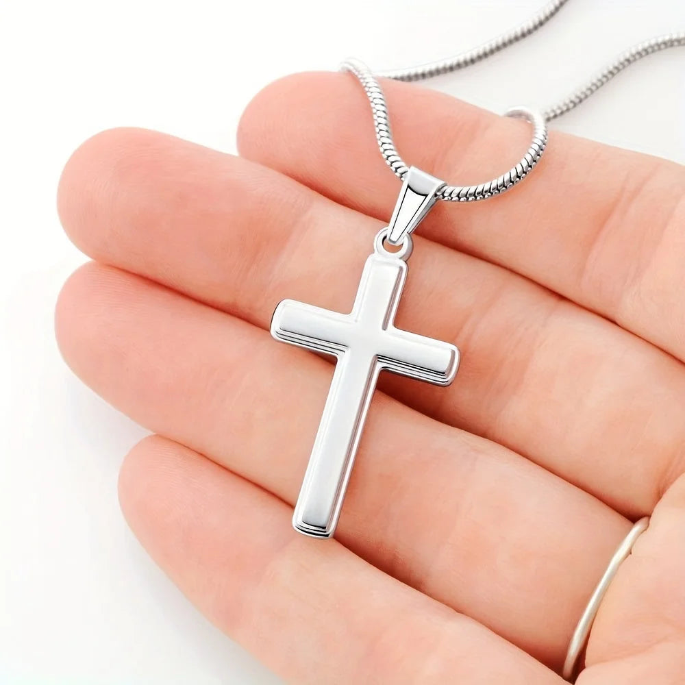 Silver cross pendant on a chain held in a hand against a white background
