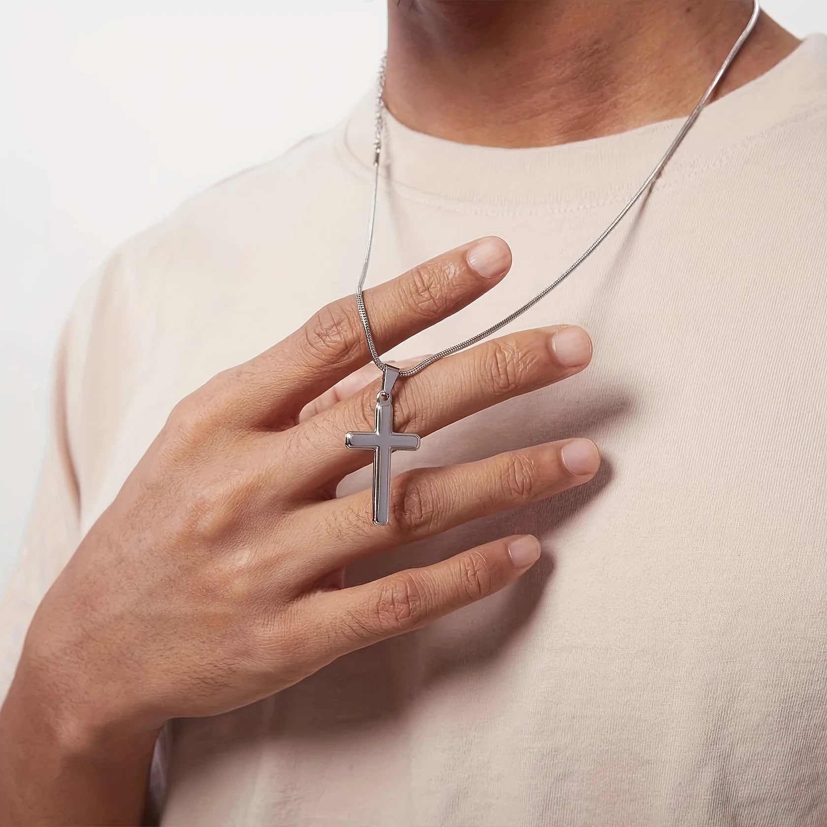 Person wearing a silver cross necklace with a neutral background