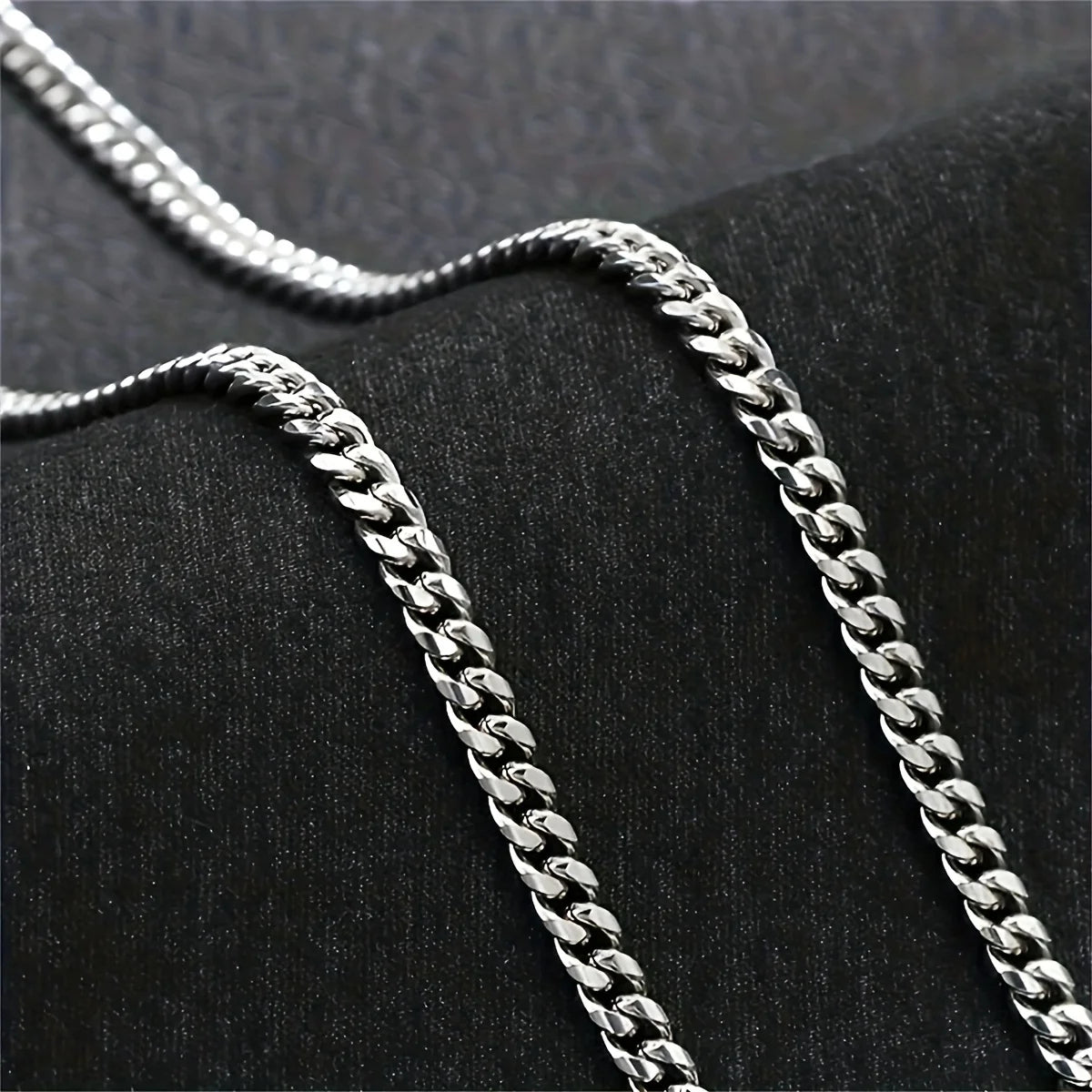 Two silver chains on a black textured surface