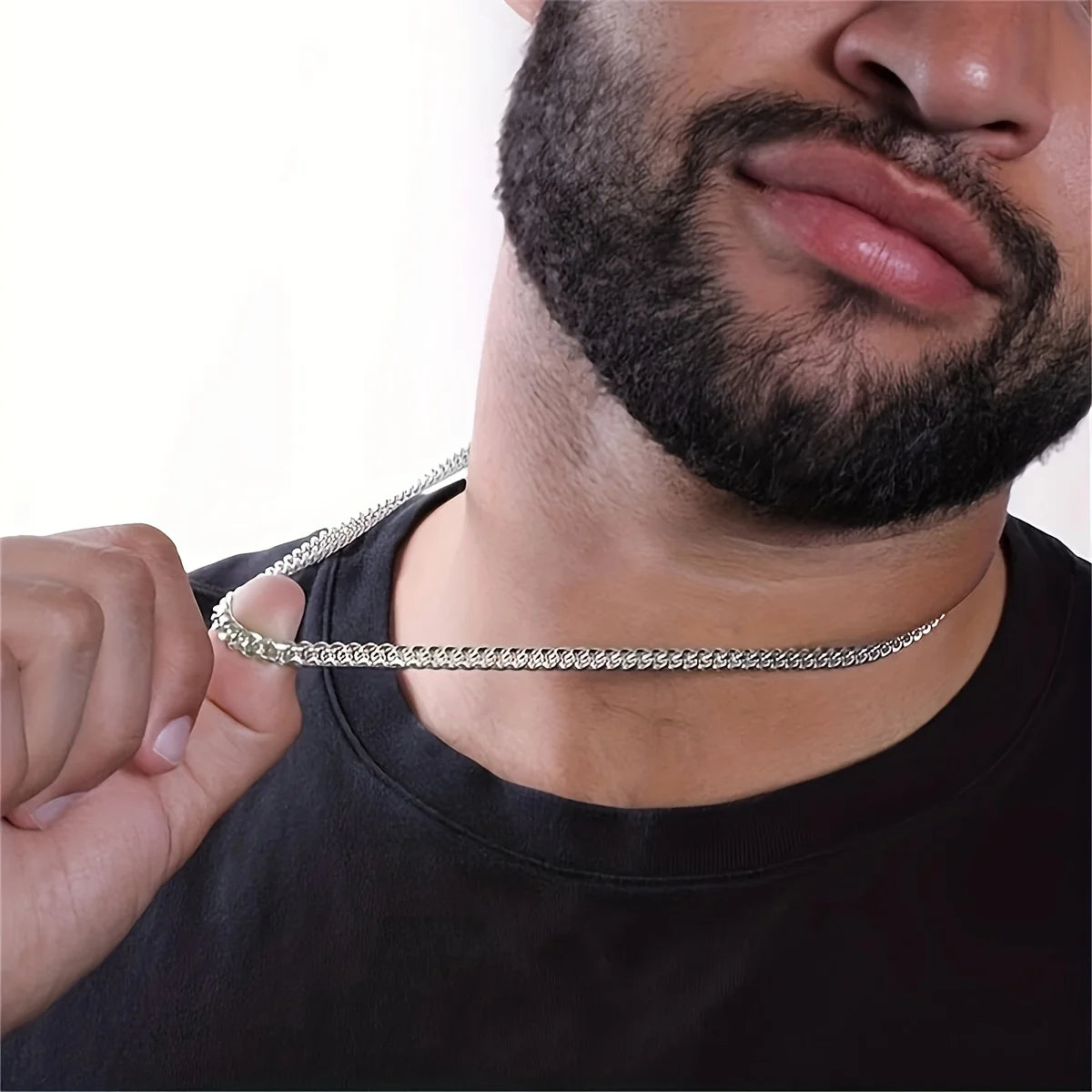 Man wearing a silver chain necklace against a plain background