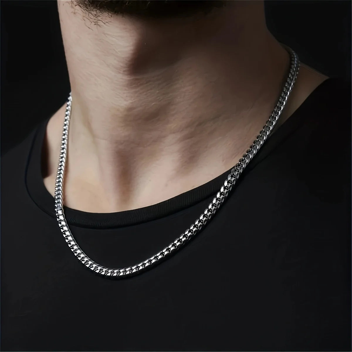 Silver chain necklace worn by a person on a black background