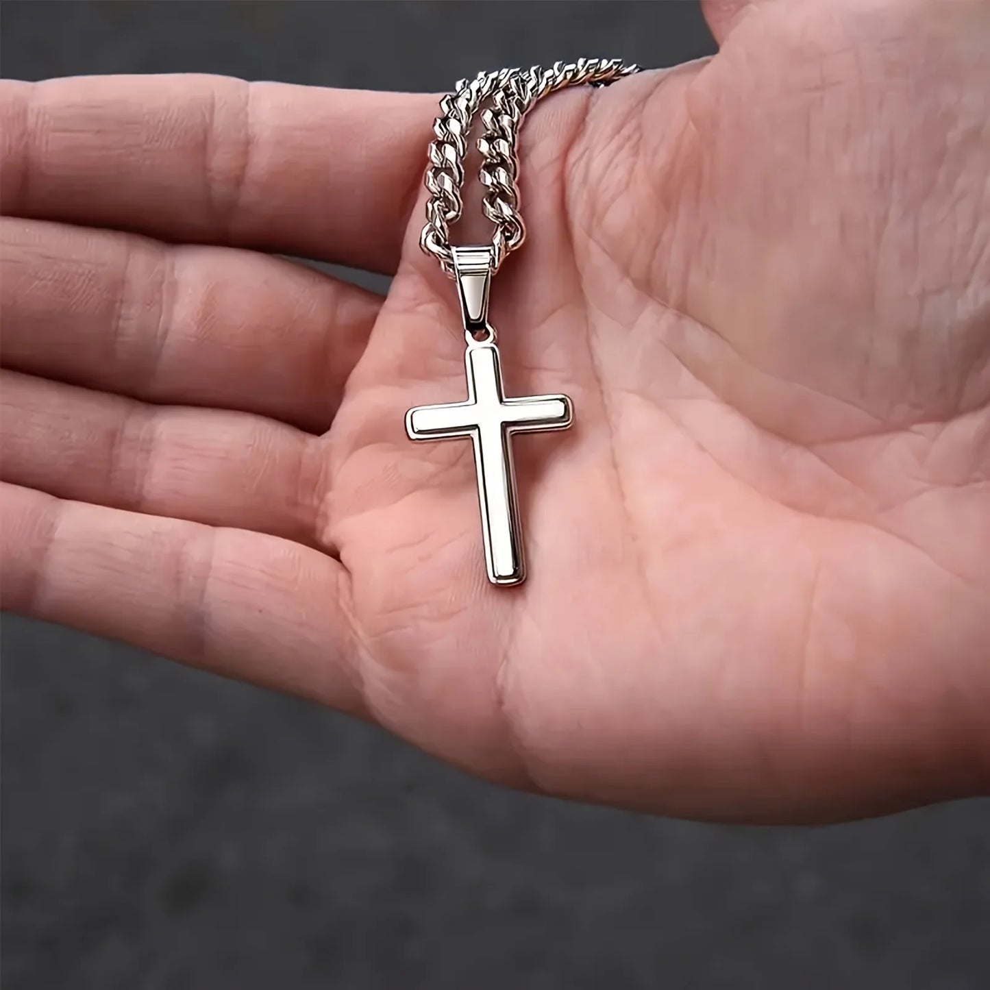 Silver cross pendant on a chain held in a hand against a dark background