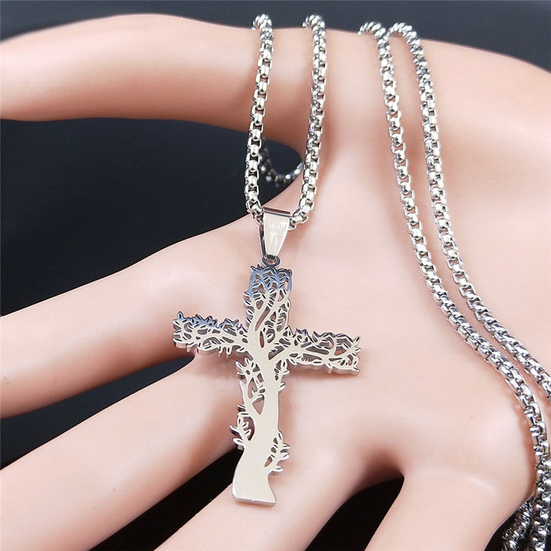 Silver cross necklace with tree design on a hand against a dark background