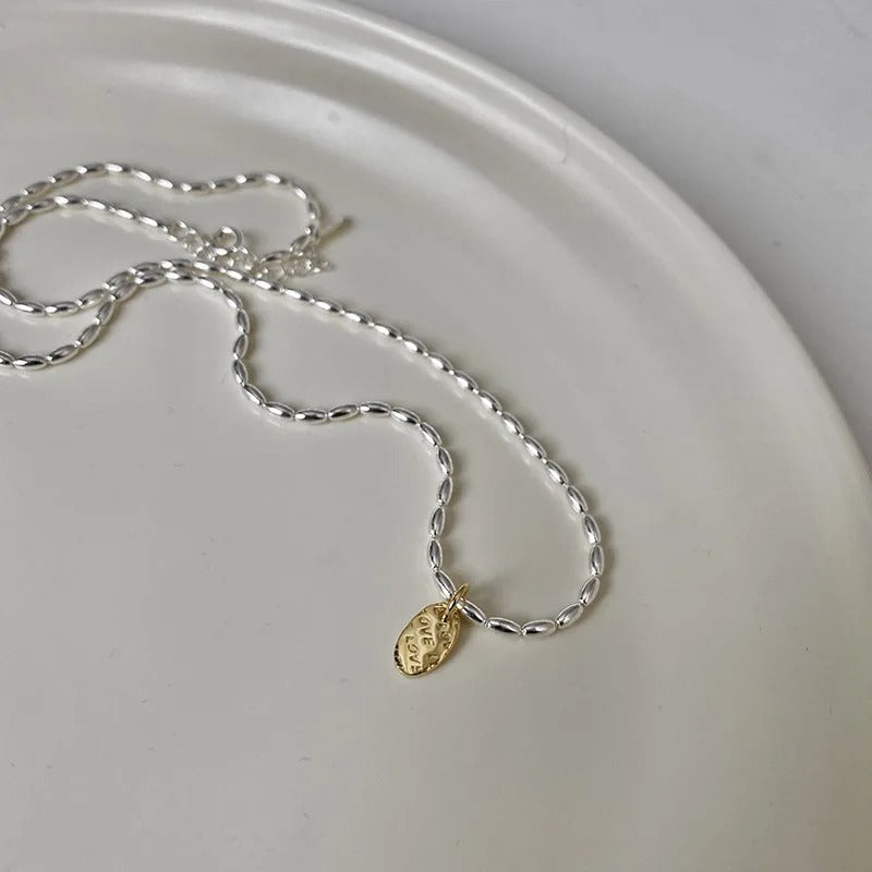Silver necklace with a gold pendant on a white plate