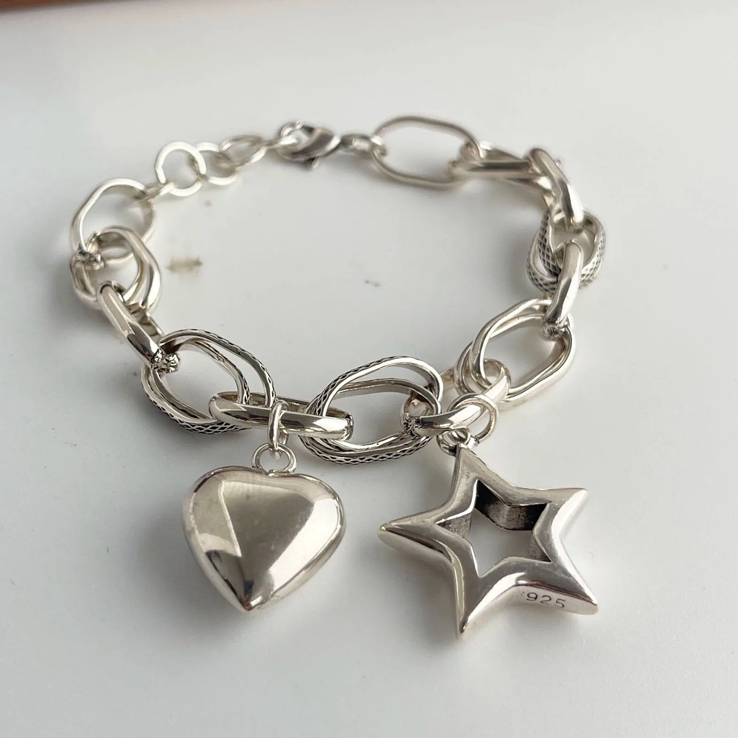 Silver chain bracelet with heart and star charms on a white background
