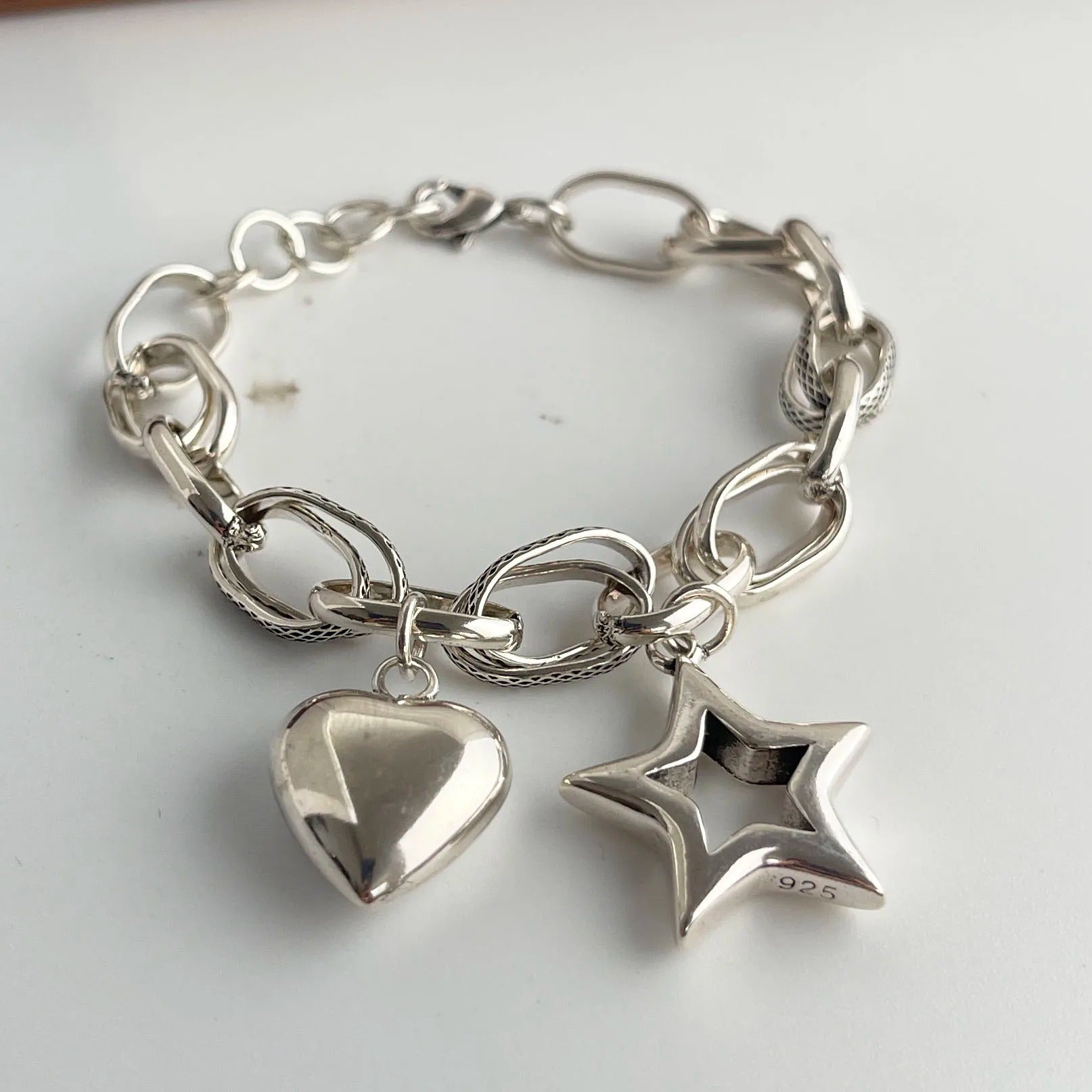 Silver chain bracelet with heart and star charms on a white background