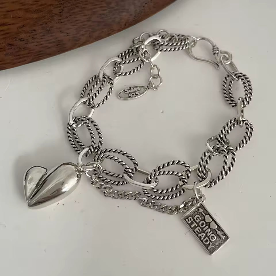 Silver chain bracelet with heart and rectangular charm on a white surface