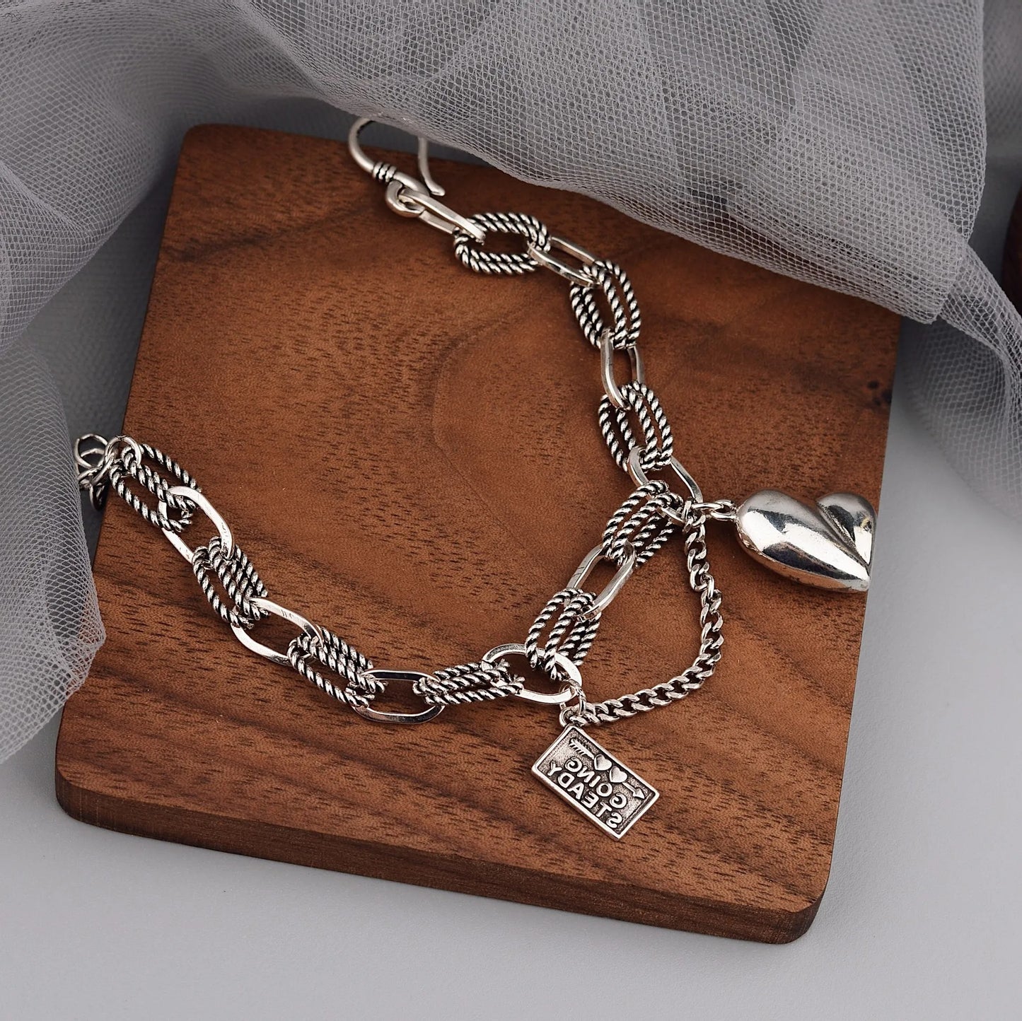 Silver chain necklace with heart charm on a wooden stand