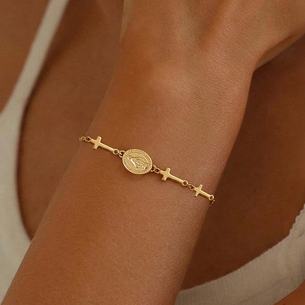 Gold bracelet with religious symbols on a wrist against a neutral background