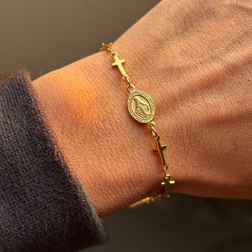 Gold bracelet with religious charms on a wrist against a neutral background
