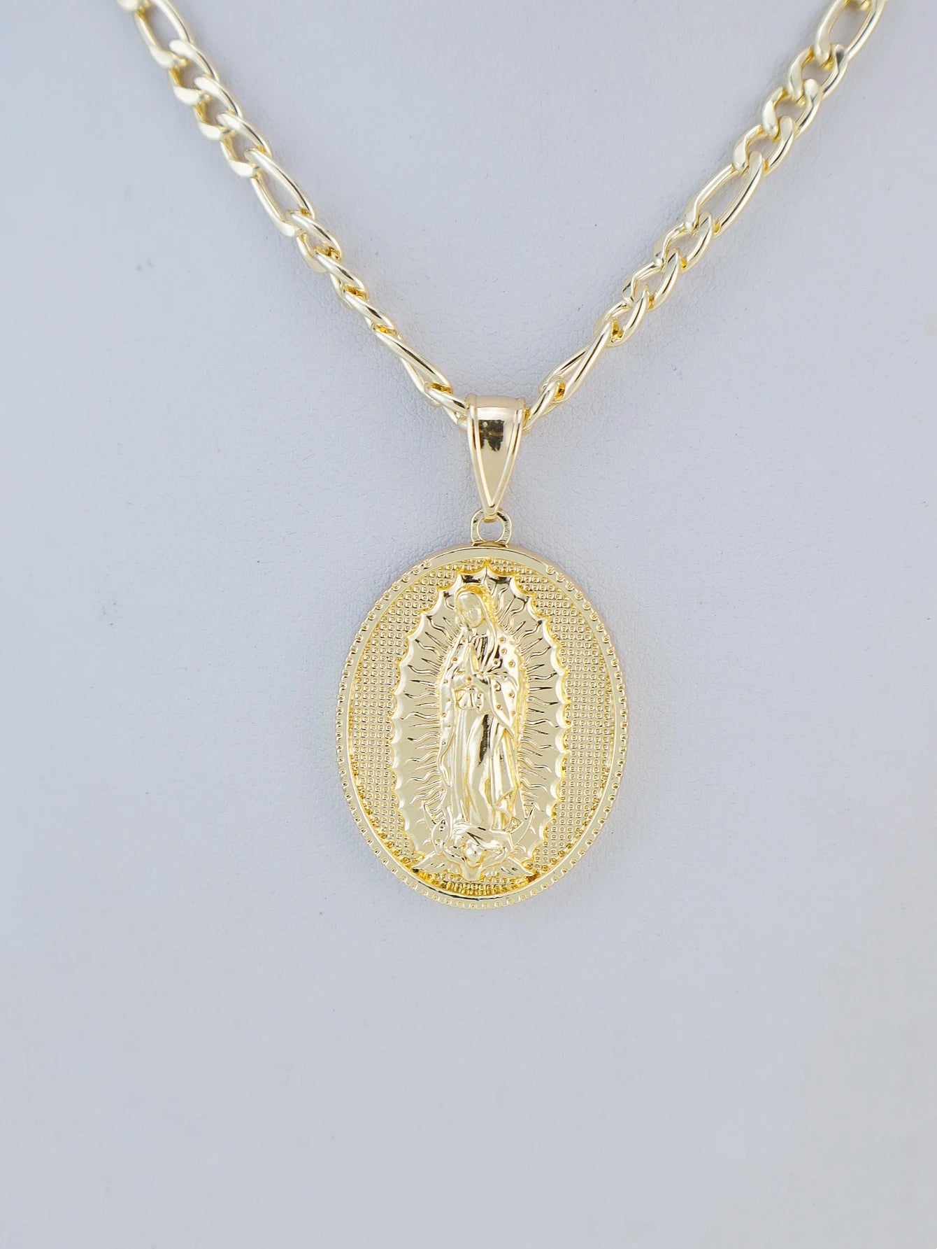 Gold necklace with a religious pendant on a light gray background