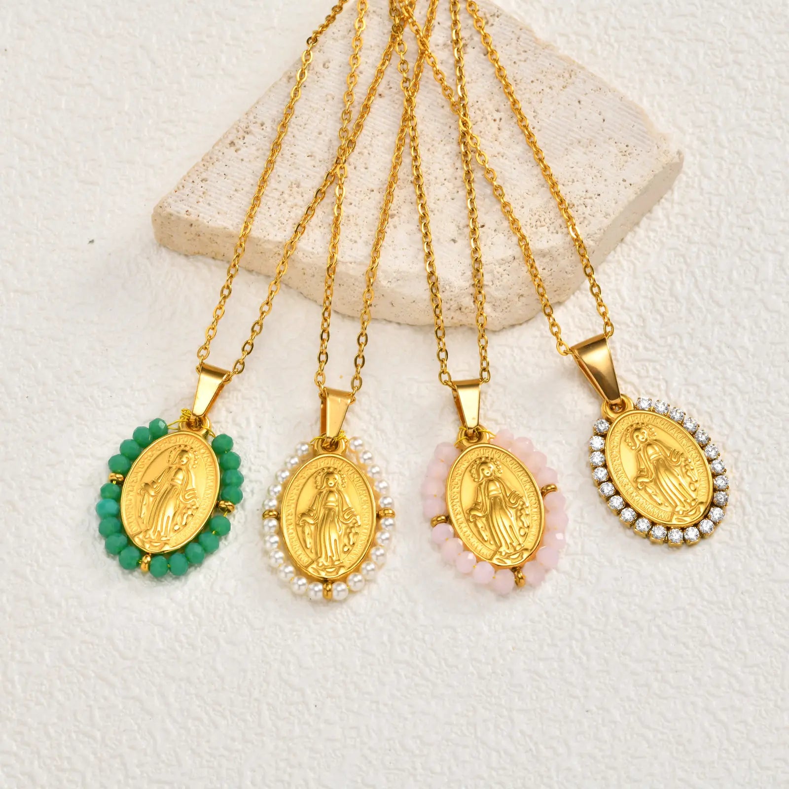 Four gold necklaces with religious pendants on a textured white surface