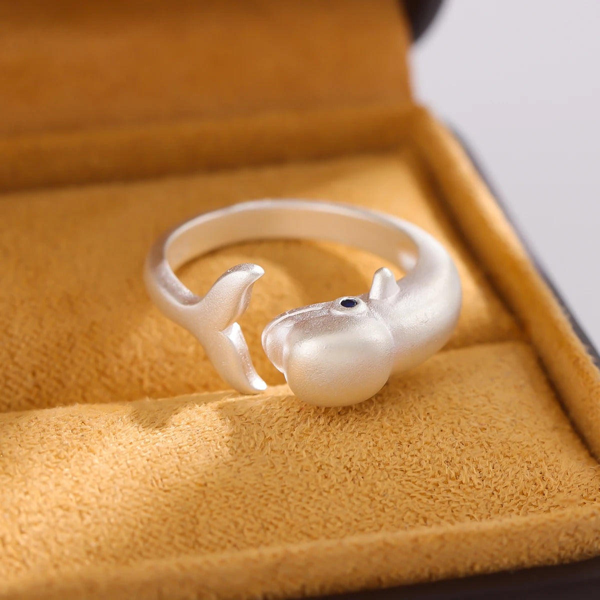 Silver whale-shaped ring on a yellow fabric surface
