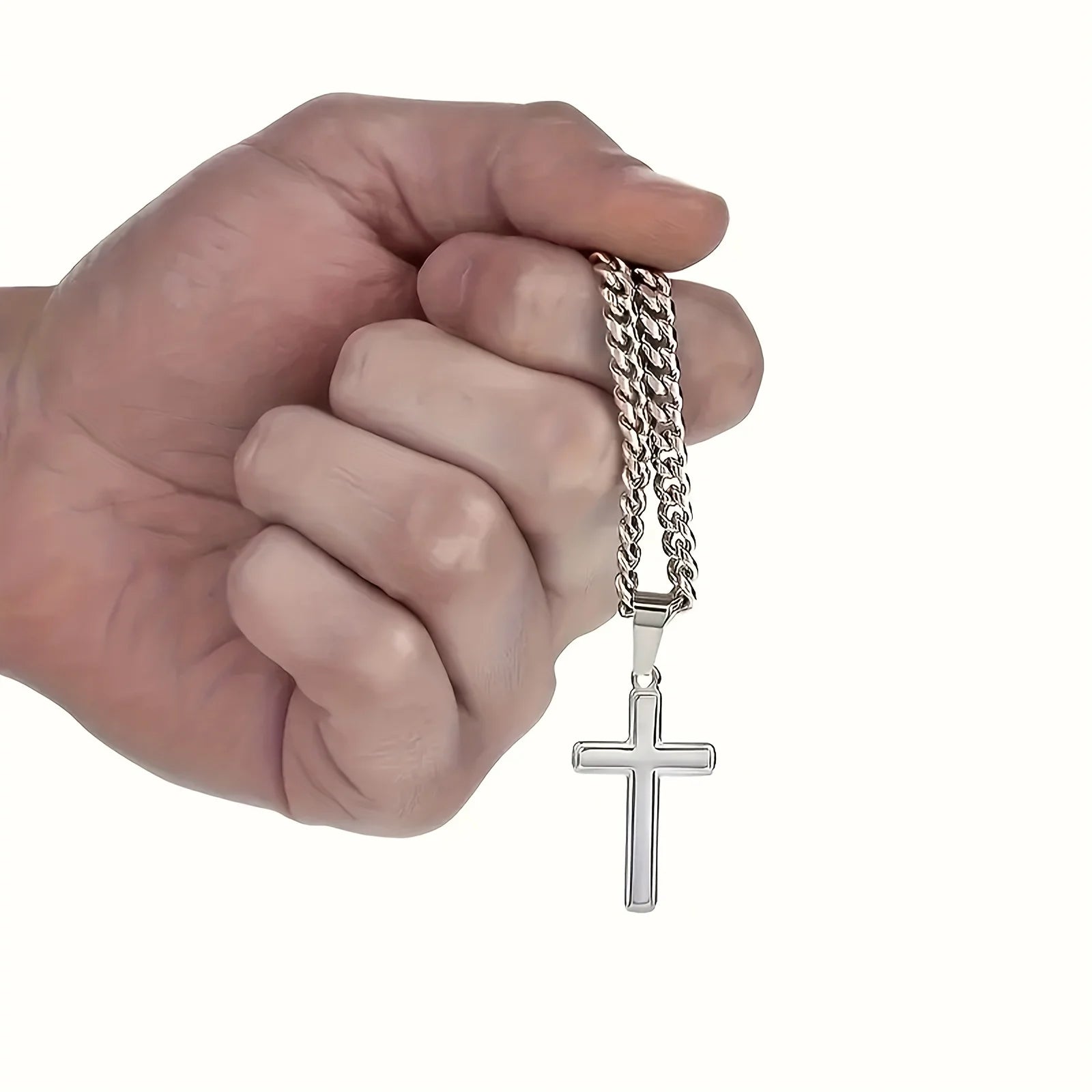 Hand holding a silver chain with a cross pendant on a white background