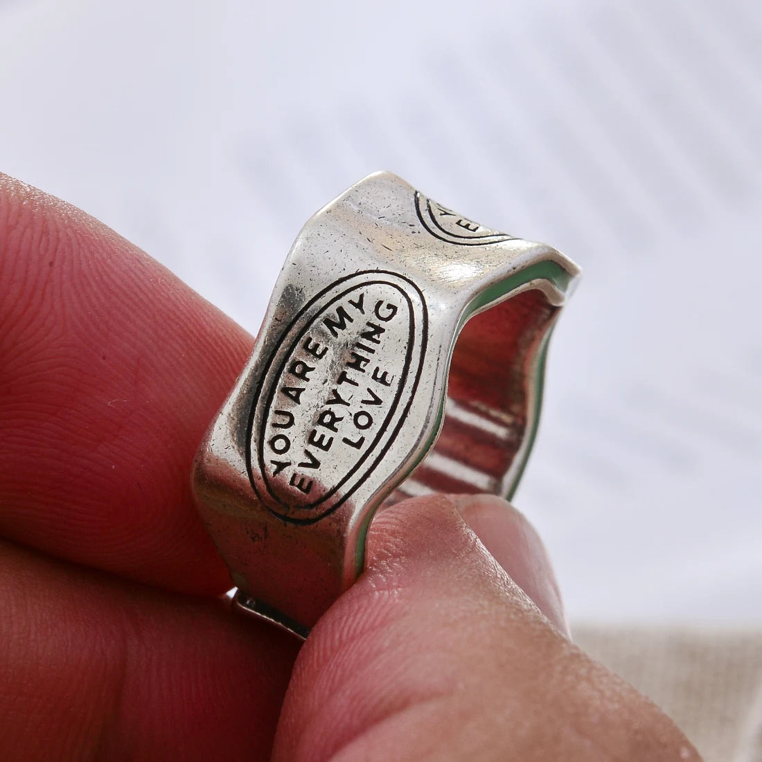 Silver ring with 'You Are My Everything Love' engraving held between fingers against a blurred background