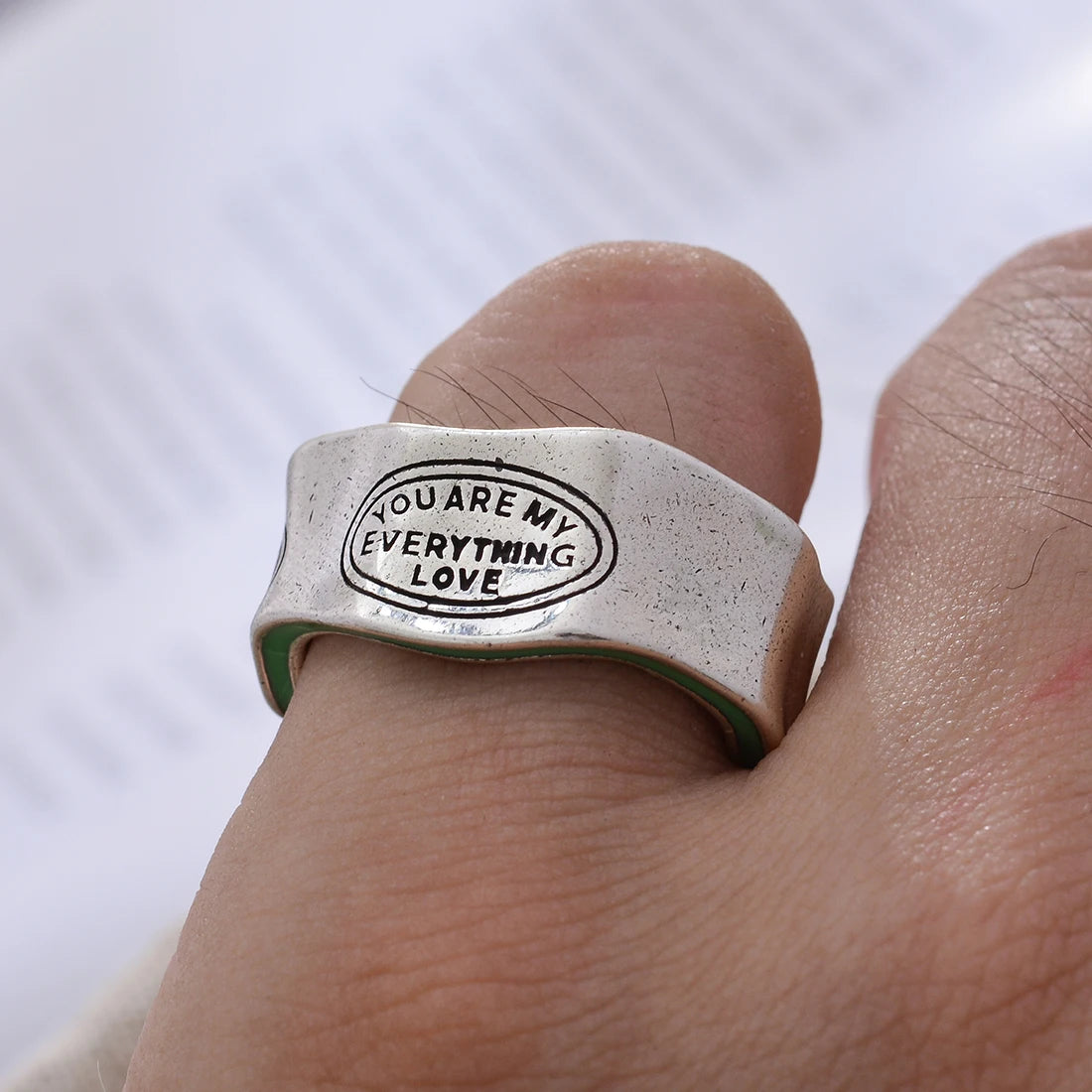 Silver ring with 'YOU ARE MY EVERYTHING LOVE' engraving on a finger against a white background